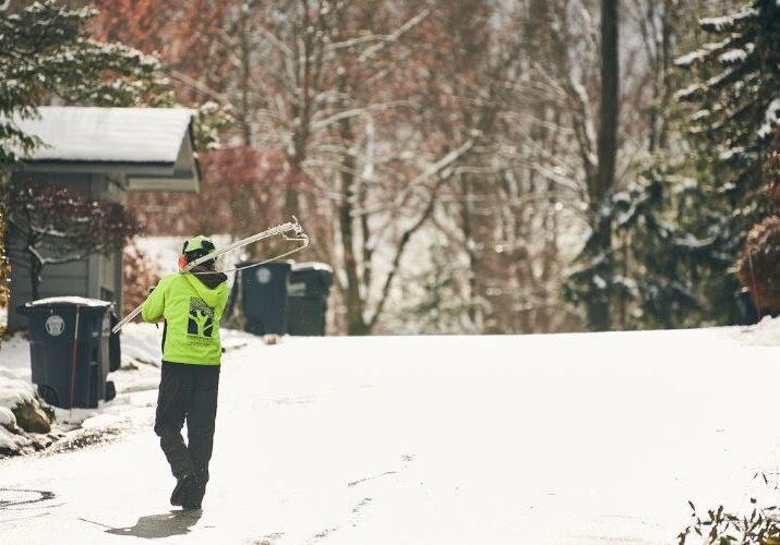 An Independent Tree crew member carries a pruning tool through a wintry scene with snow and trees in Ohio.