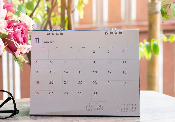 A desk calendar in front of a backyard with green trees and near a bouquet of cut flowers.