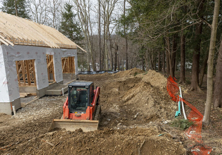 Construction equipment, the frame of a new building, and piles of dirt near a grove of trees